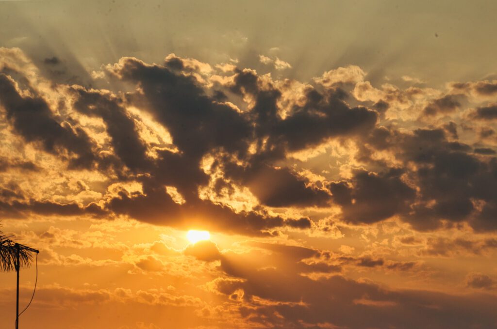 O céu exibe uma gama de cores que se estende do laranja ao azul amarelado, marcando a transição para o amanhecer. Sua beleza é vista em vários olhares.